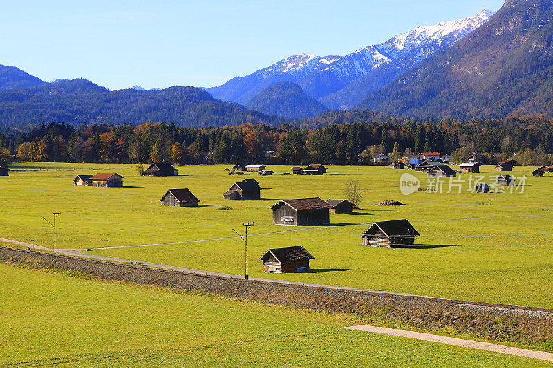 在谷仓农场和小木屋之上，阳光明媚的Garmisch Partenkirchen阿尔卑斯村庄在巴伐利亚阿尔卑斯山从Alpspitze，田园诗般的松树林地秋季景观，雄伟的阿尔卑斯山谷，戏剧性的巴伐利亚德国雪山全景，德国